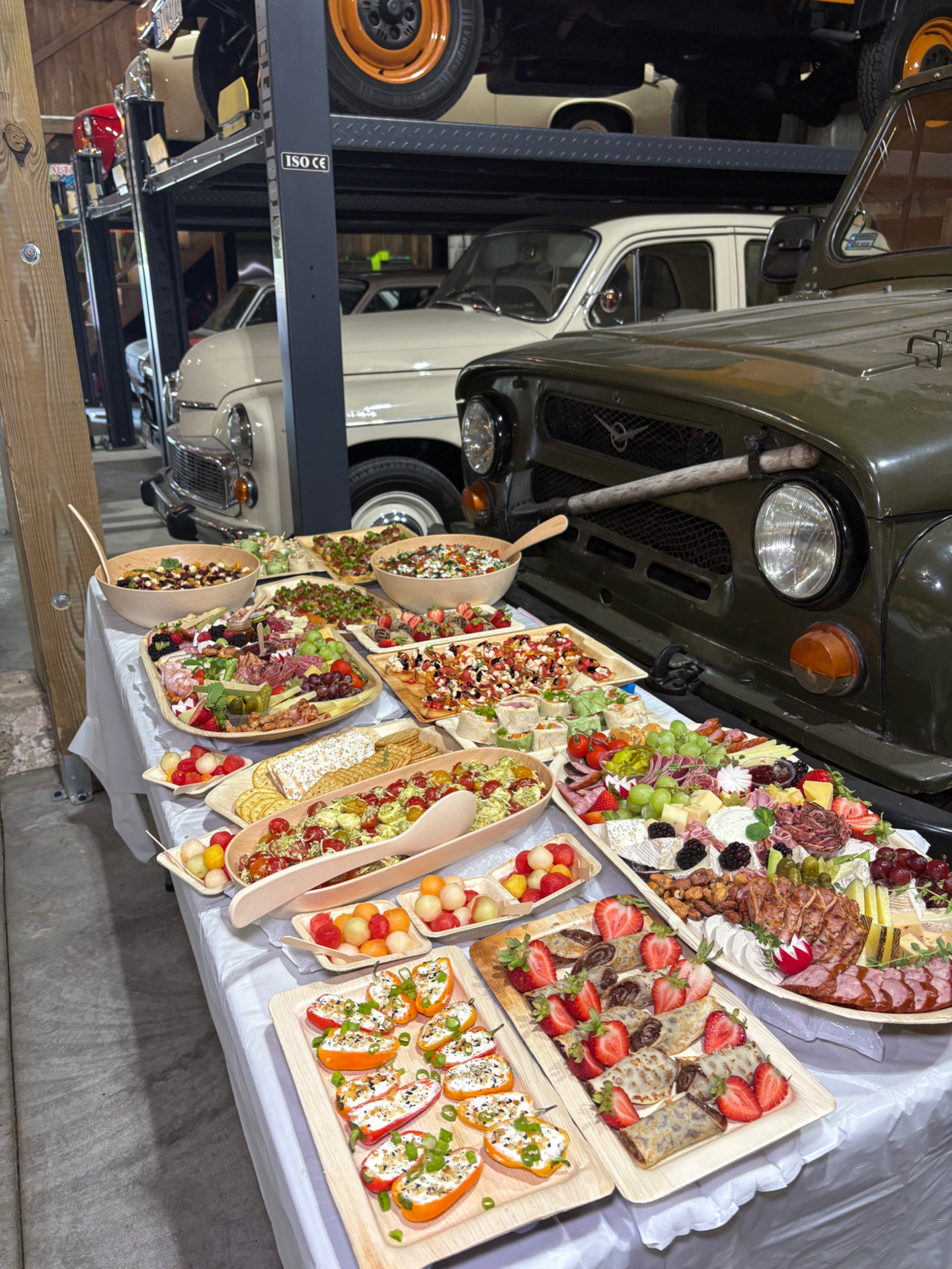 Birthday party grazing spread with charcuterie boards, bruschetta, pinwheels, and chocolate-filled crepes among vintage cars