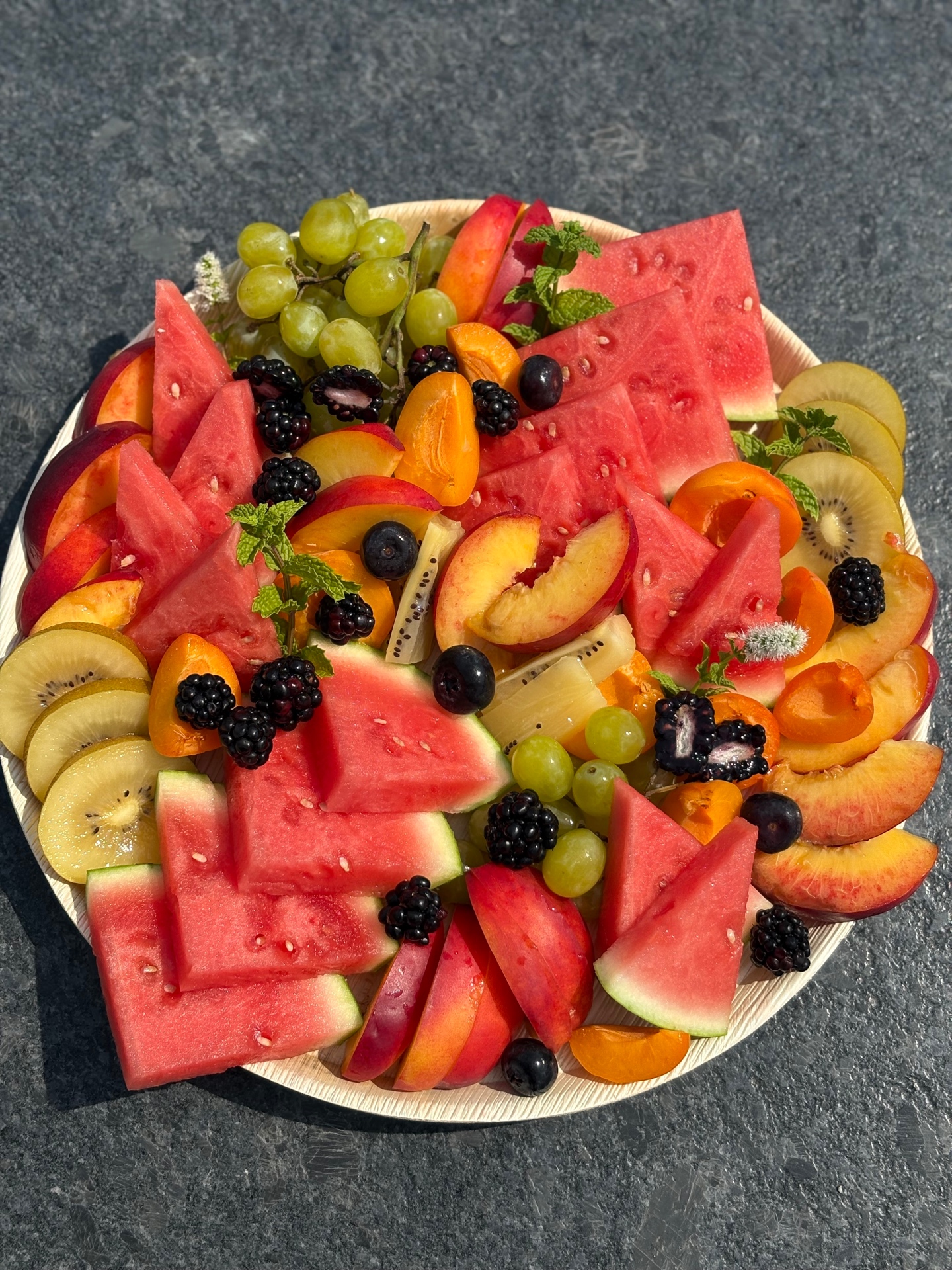 Fresh fruit platter with watermelon, nectarines, kiwi, grapes, apricots, blackberries, and mint