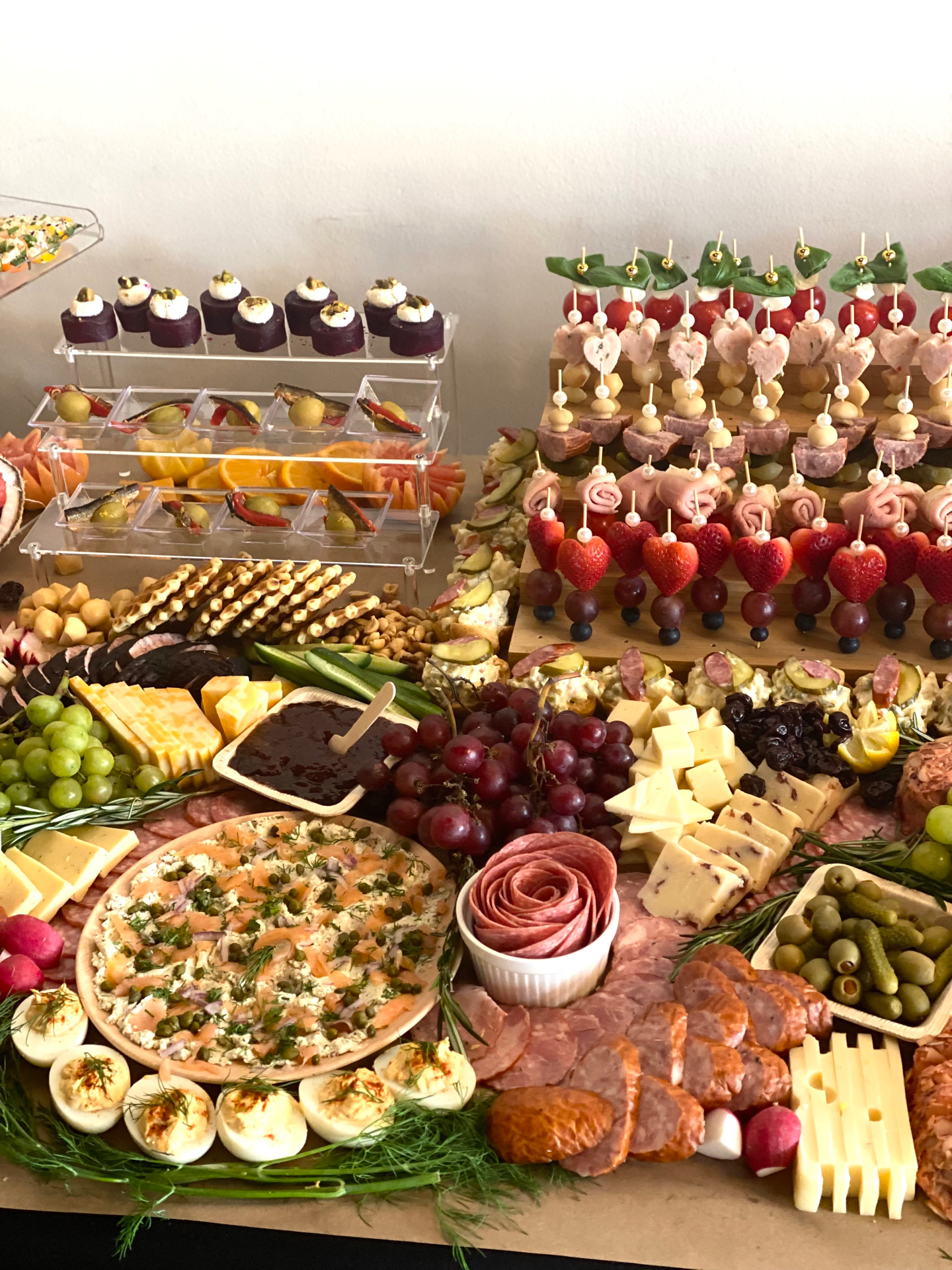 Baby shower grazing table with heart-shaped strawberry skewers, a smoked salmon dip platter, deviled eggs, and cheeses
