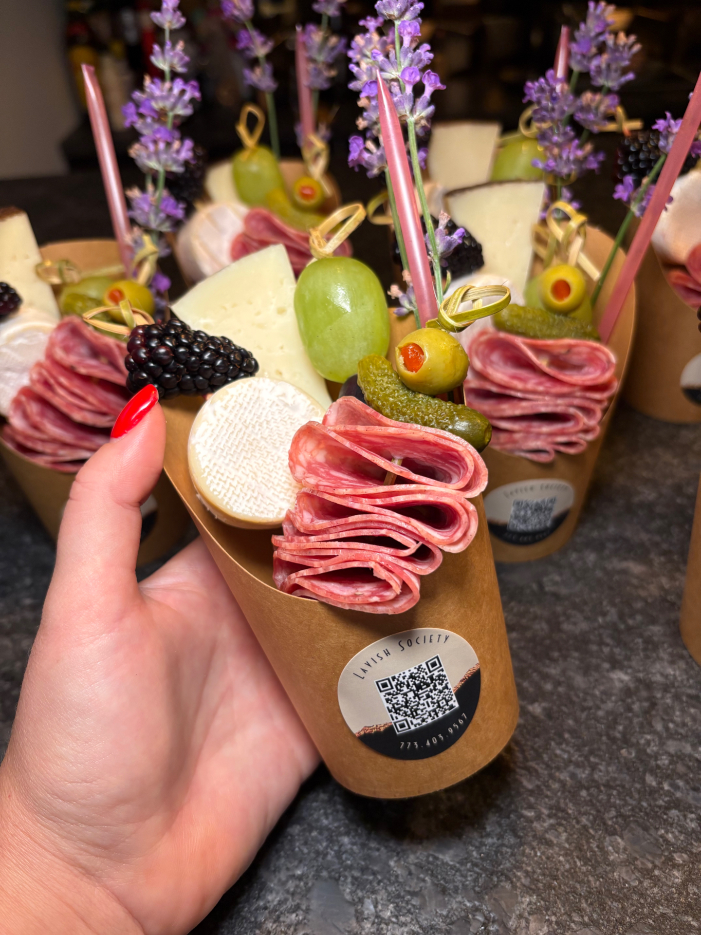 Individual charcuterie cup with salami ribbons, cheese, olives, and lavender in a branded Lavish Society cup
