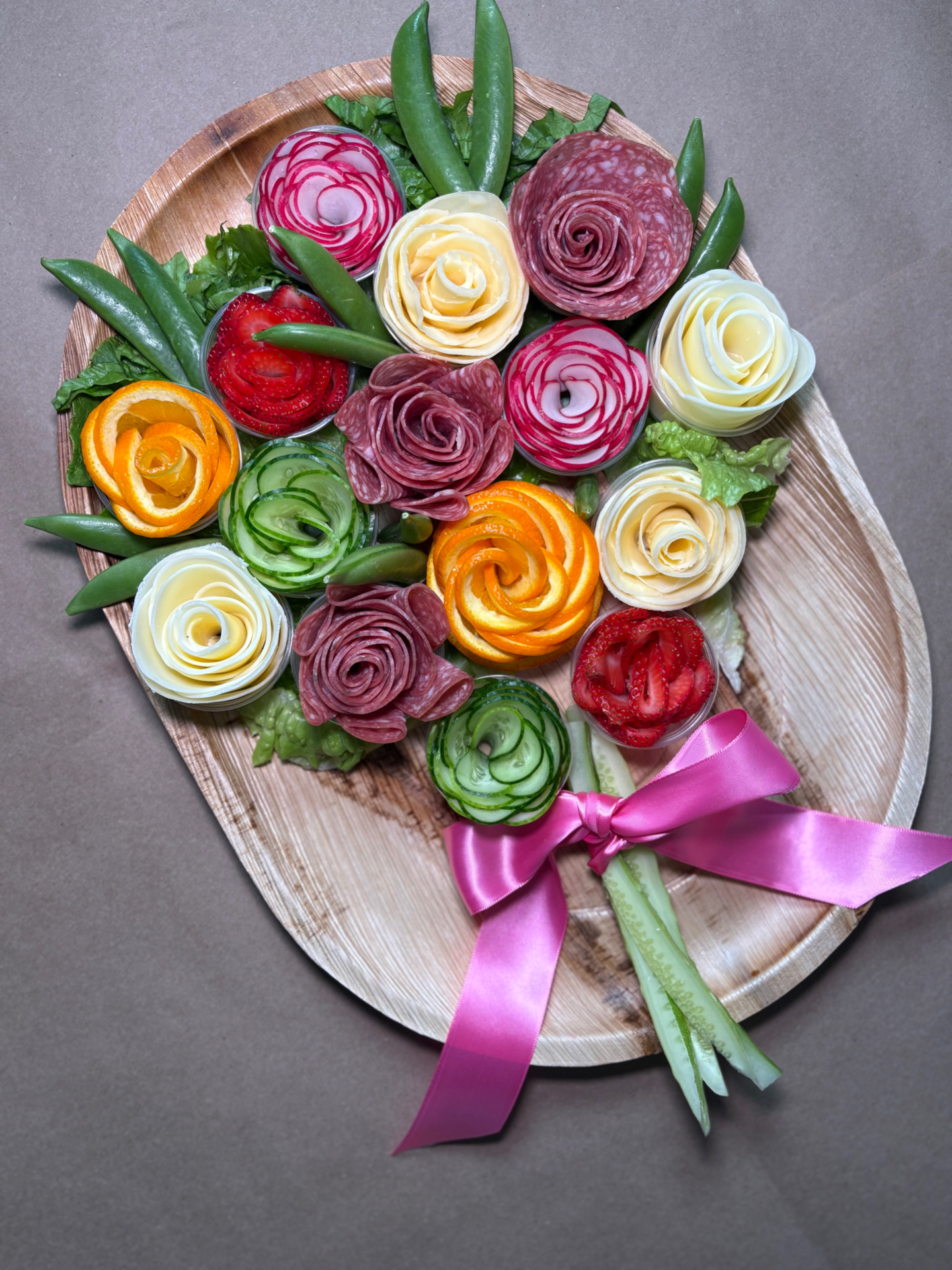 Charcuterie bouquet with salami, cheese, radish, cucumber, and orange roses tied with a pink ribbon