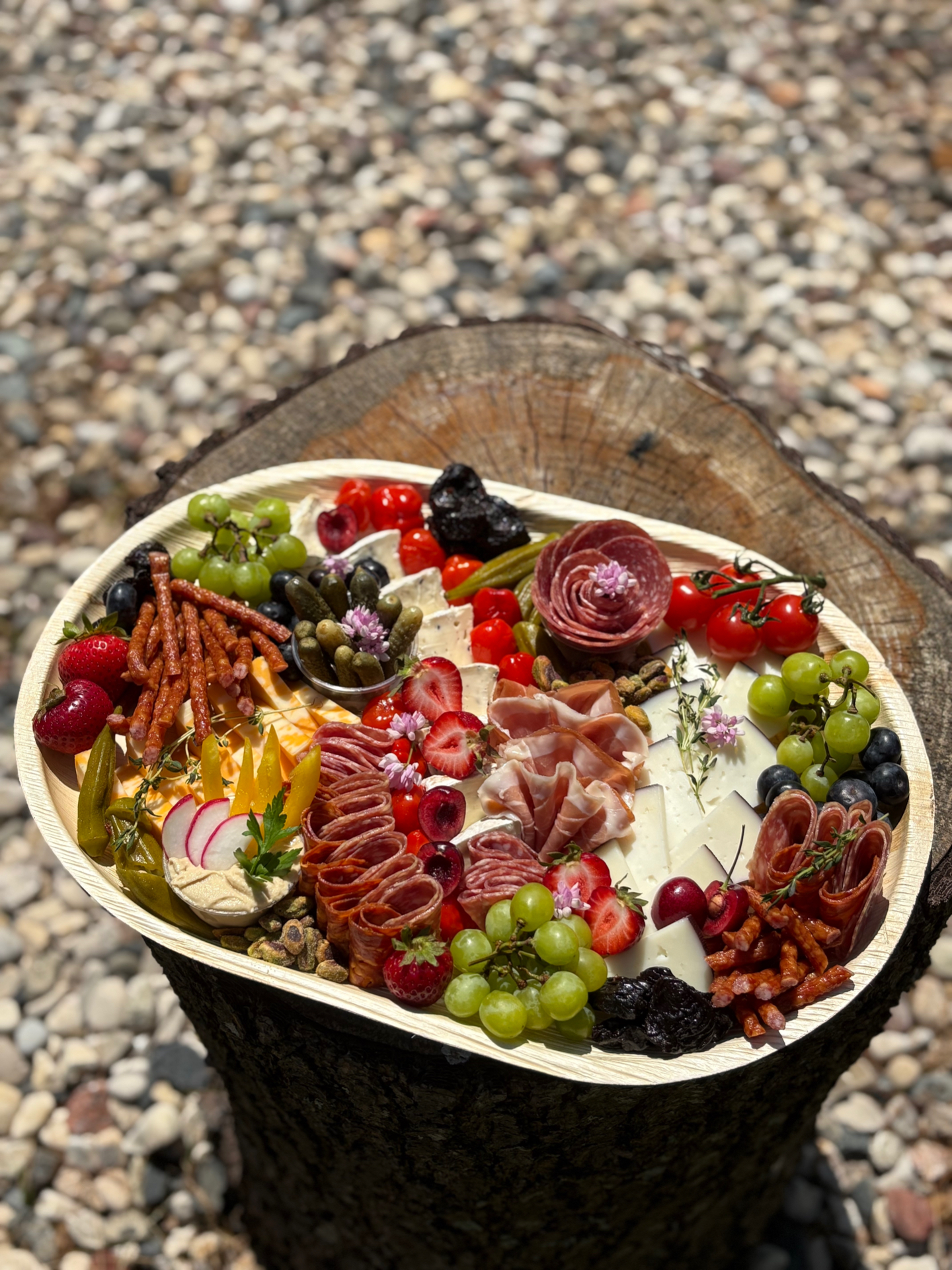 Medium charcuterie board with salami rose, prosciutto, cheeses, grapes, and berries on a palm leaf tray