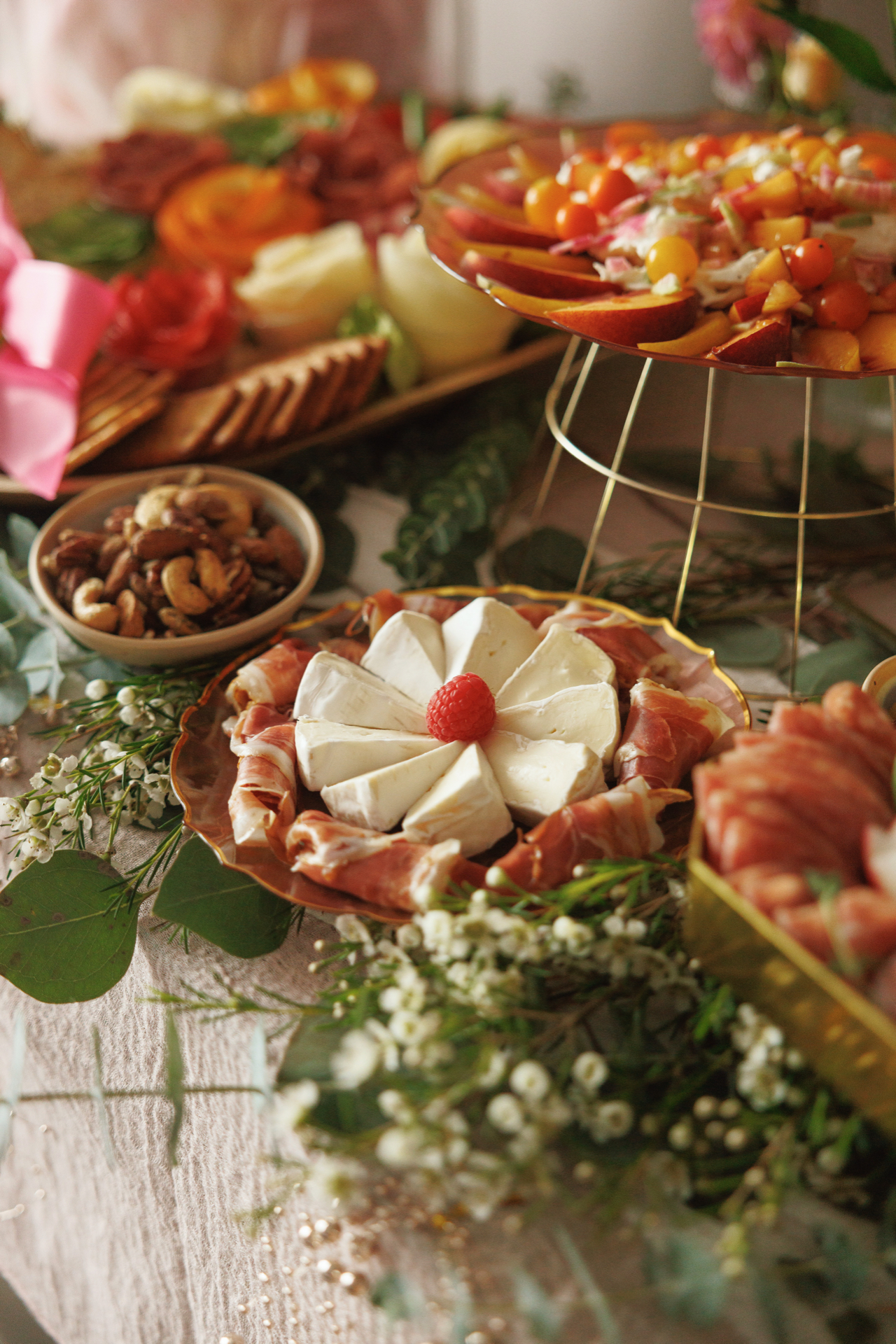 Brie wedges arranged as a flower with a raspberry center, wrapped in prosciutto on a gold-rimmed plate