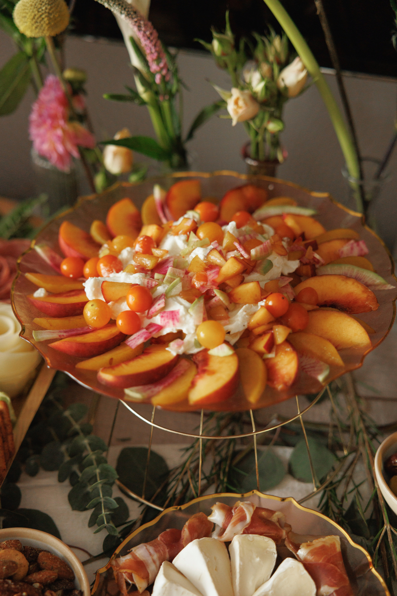 Peach and burrata salad with sungold tomatoes and watermelon radish on an amber glass cake stand