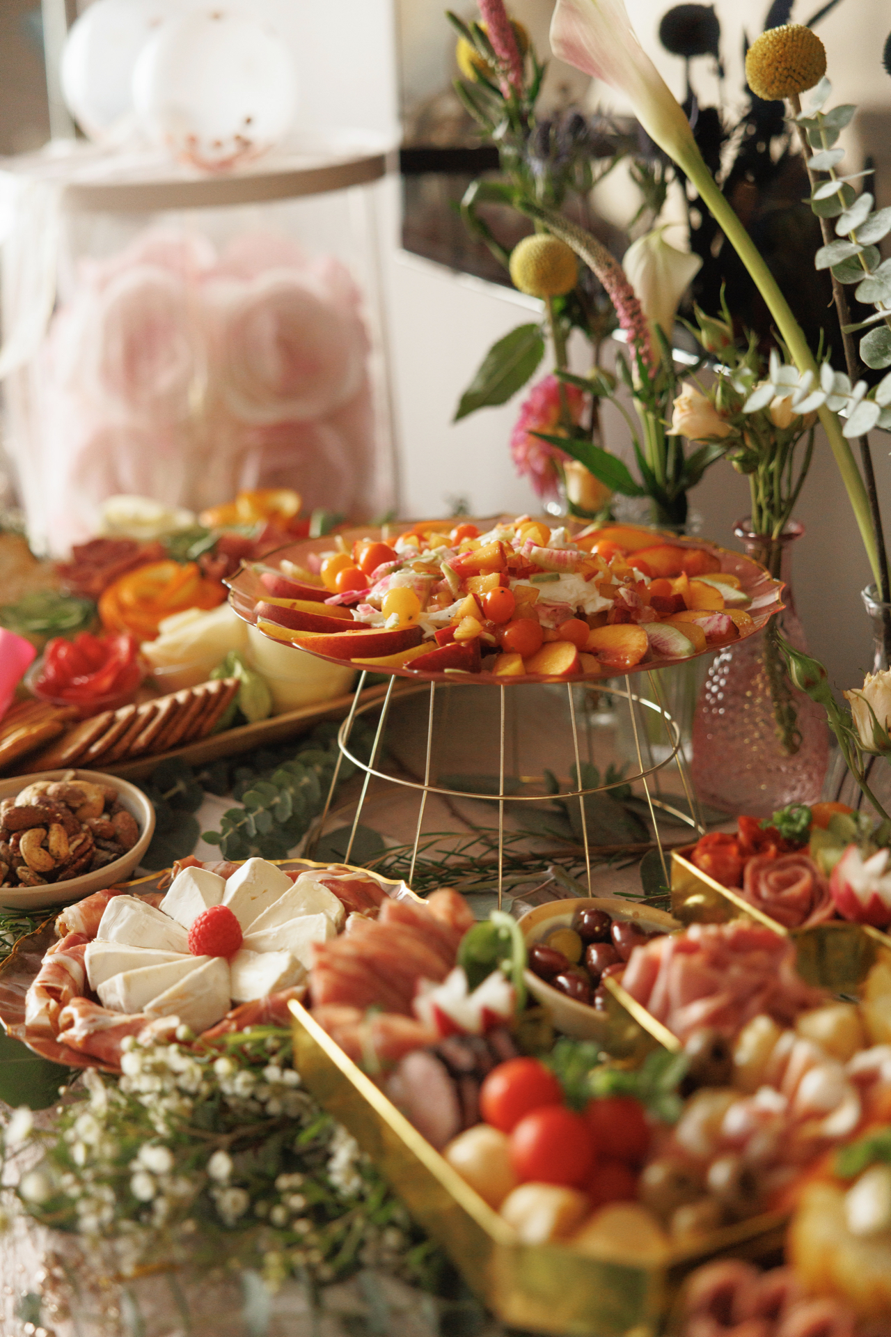 Bachelorette party table with peach burrata salad, a brie flower plate, and charcuterie trays in warm light